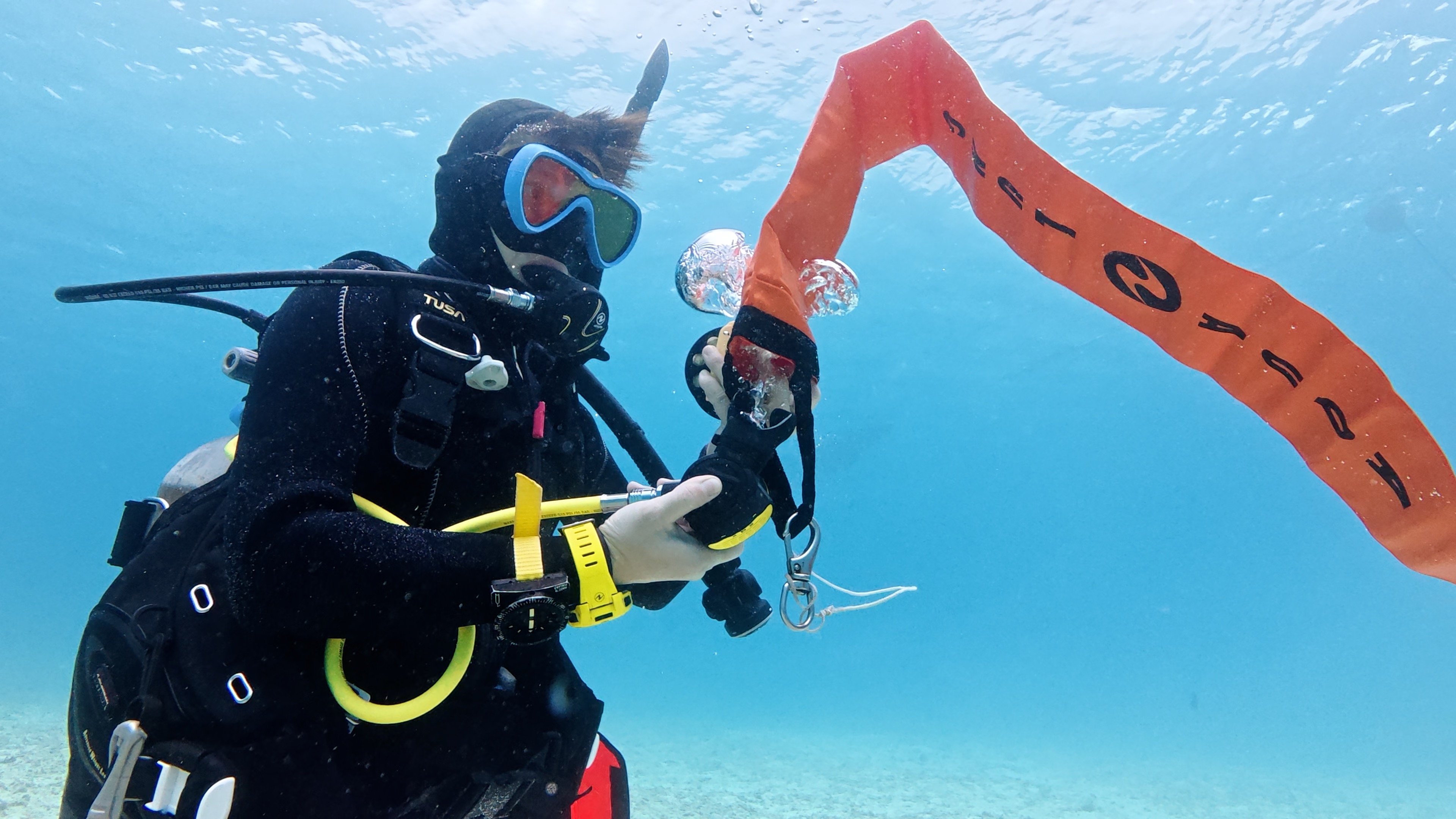 沖縄・恩納村の海中でダイバーがオレンジ色のシグナルフロート（SMB）の使い方を練習している様子